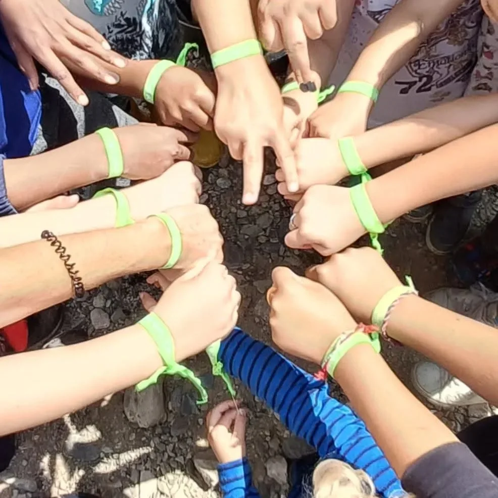 Educació ambiental Un grup reuneix les mans amb polseres verdes durant una activitat a l’aire lliure.