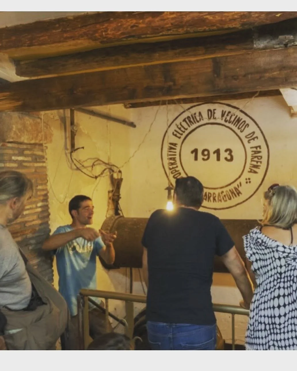 Patrimoni de Farena Un guia explica el patrimoni hidràulic a un grup al costat del rètol de la cooperativa elèctrica de Farena de 1913.