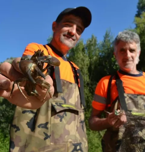 Dues persones equipades amb botes de pescador mostren un cranc i una xarxa durant un treball de camp.